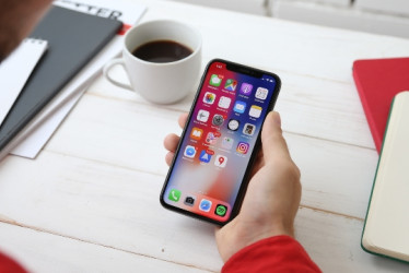 Hombre mirando su iPhone en un escritorio al lado de un cuaderno y un café.