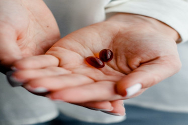 Manos de una mujer con dps cápsulas de vitaminas rojas.