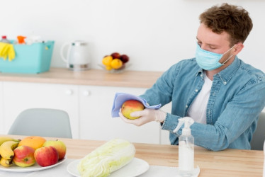 Hombre usando tapabocas desinfecta frutas con un pañuelo.