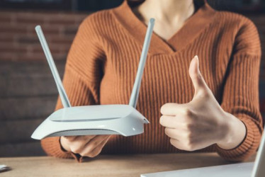 Mujer sostiene un router y hace el signo de aprobación con la otra mano.