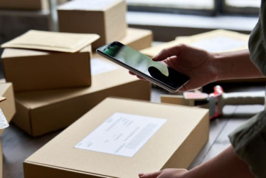 Persona con un celular escanea un código de barras en una caja de cartón.