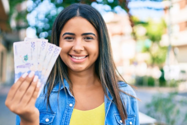 Mujer sonriendo mostrando billetes de Colombia en su mano derecha.