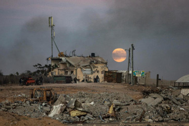 ersonas desplazadas caminan cerca de edificios destruidos mientras la luna llena se eleva sobre Khan Yunis, en el sur de la Franja de Gaza