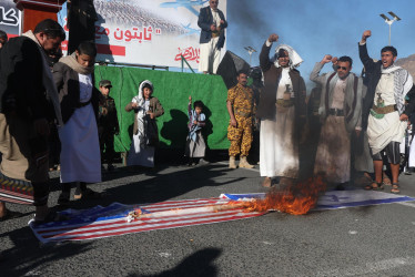 Partidarios hutíes queman una pancarta con banderas estadounidenses e israelíes durante una protesta contra esos países en Yemen.