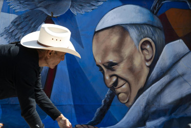 Fieles cuelgan una pancarta que representa al Papa Francisco al pie de la estatua de Juan Pablo II a la entrada del Hospital Gemelli, donde está hospitalizado.