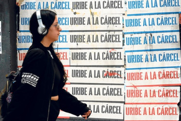 Una mujer camina frente a carteles en contra del expresidente de Colombia Álvaro Uribe, en Bogotá.