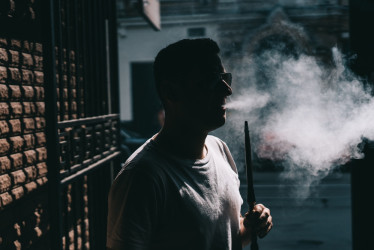 Silueta del fabricante de la cachimba que sopla humo en la oscuridad.