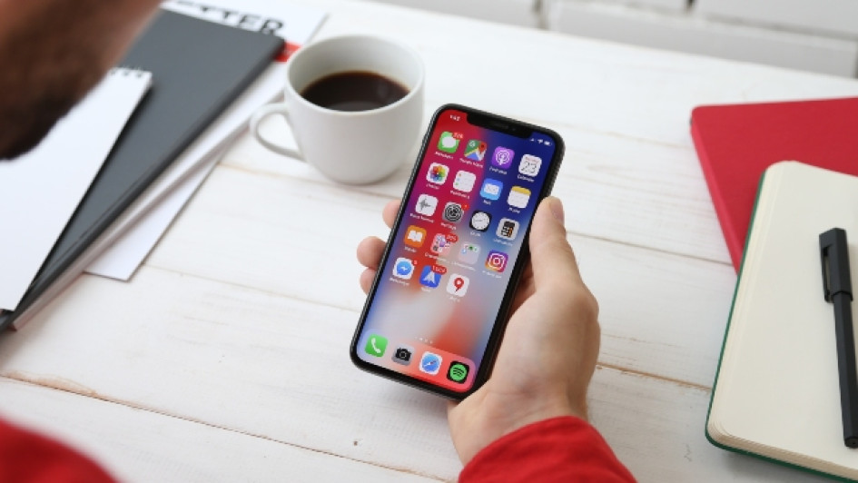 Hombre mirando su iPhone en un escritorio al lado de un cuaderno y un café.