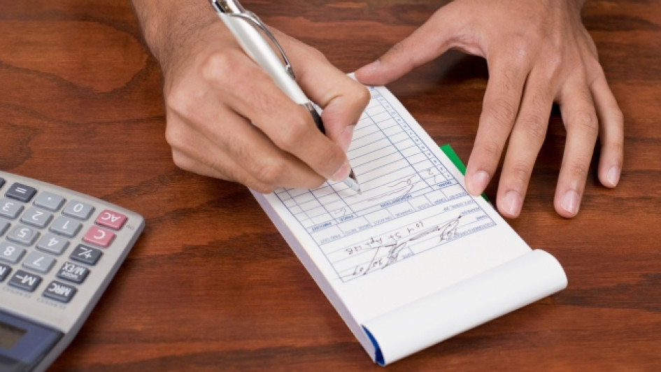 Mano llenando un recibo de caja al lado de una calculadora.