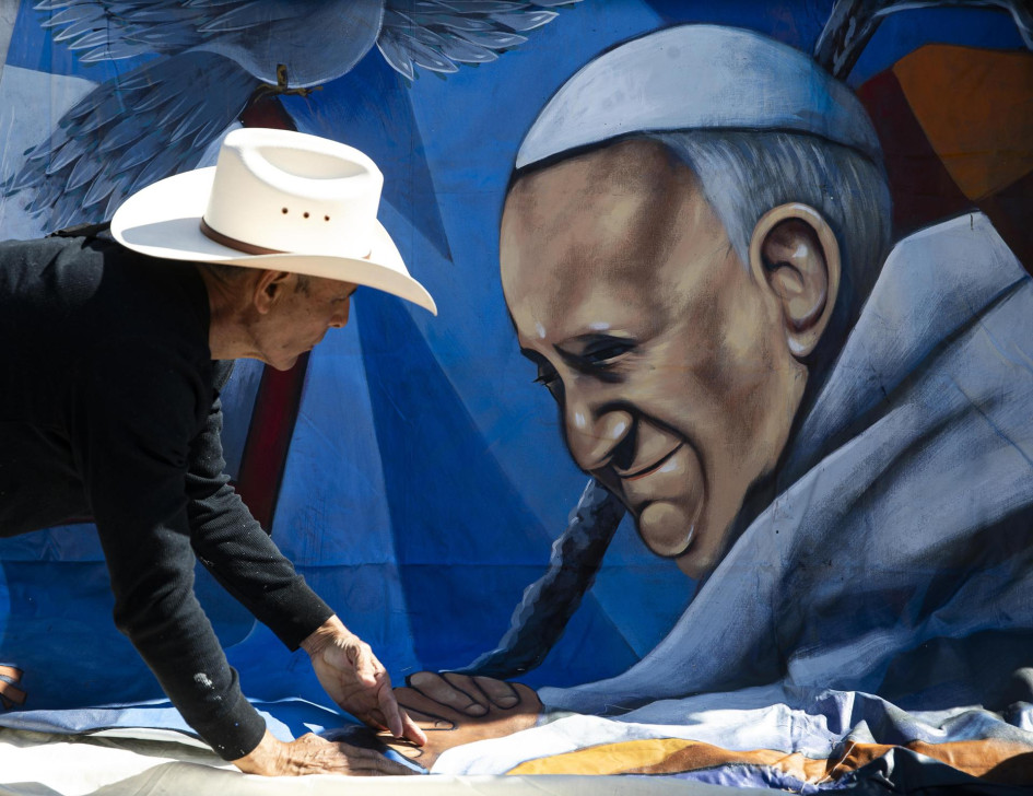 Fieles cuelgan una pancarta que representa al Papa Francisco al pie de la estatua de Juan Pablo II a la entrada del Hospital Gemelli, donde está hospitalizado.